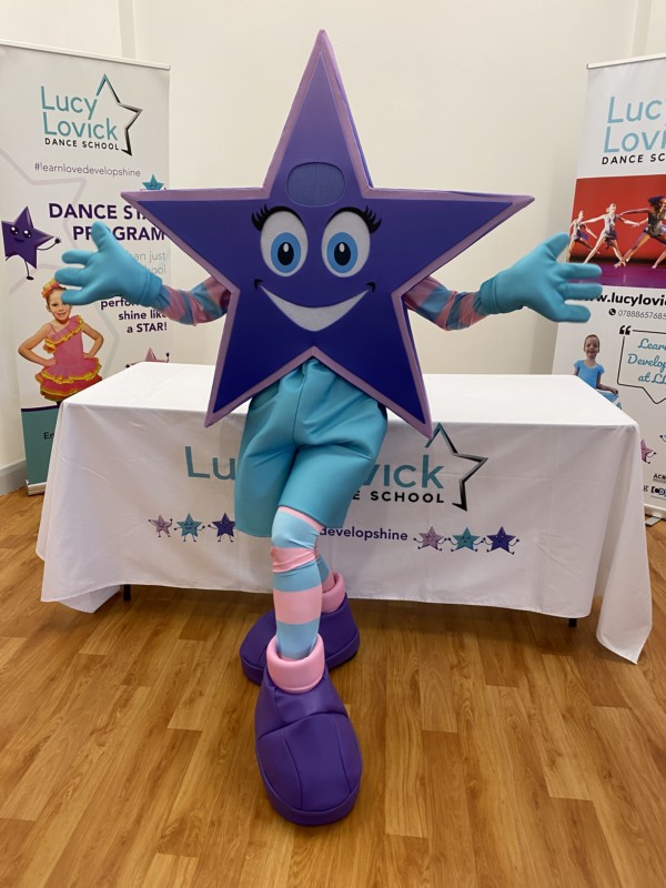 The Lucy Lovick Dance Studio star mascot posing in front of branded studio banners