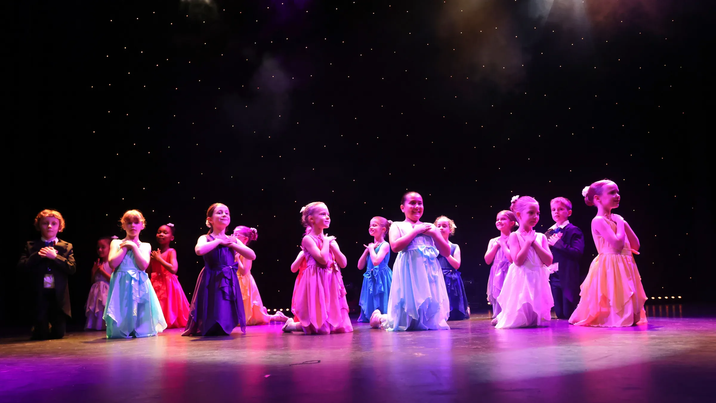 Young dancers in colourful dresses performing on stage at the studio show
